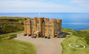 a large building on a hill with the ocean in the background at Camelot Castle Hotel in Tintagel