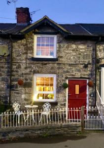 uma casa de pedra com uma porta vermelha, uma mesa e cadeiras em Maytree Cottage. Compact home in Mid Wales. em Llanrhaeadr-ym-Mochnant