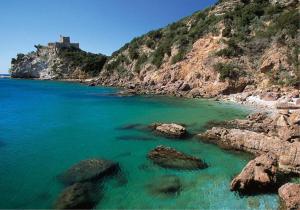 a beach with rocks and a castle on a hill at Il relax tra mare e campagna in Castiglione della Pescaia