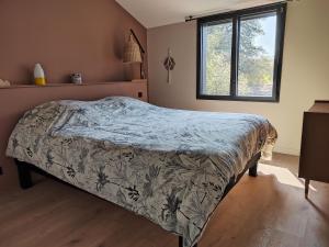 a bedroom with a bed with a comforter and a window at Joyau au cœur de la forêt in La Guérinière