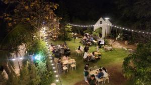 un grupo de personas sentadas en mesas en un jardín por la noche en NATA Ville - นาตาวิลล์ สระบุรี, 