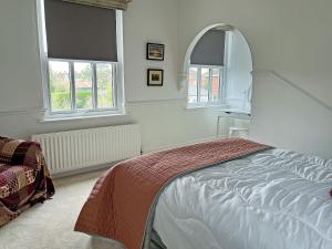 a white bedroom with a bed and two windows at Poppy Cottage in Eryholme