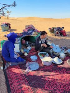 dwoje ludzi siedzących na kocu na pustyni w obiekcie Adventure dans le desert w mieście Tagounite