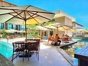 a patio with tables and umbrellas next to a swimming pool at Flat no Centro de Porto de Galinhas -SUNNY HALL120 in Porto De Galinhas