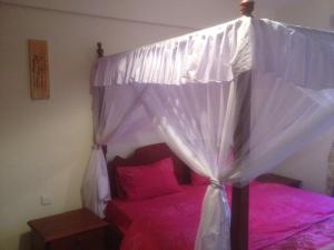 1 dormitorio con cama con dosel y sábanas rosas en Bamburi Beach Homes, en Bamburi