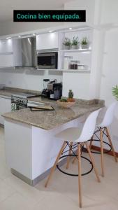 a kitchen with a counter with two white chairs at Apart. con aire, frente al mar in Porlamar