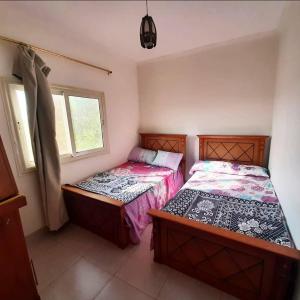 two beds in a small room with two windows at Dija's holiday rental in El-Qaṭṭa
