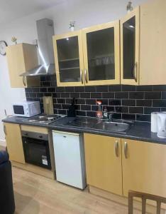 a kitchen with wooden cabinets and a black tile wall at *Cosy 1 bedroom apt nxt to Roundhay and centre * in Roundhay