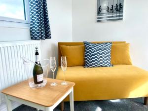 a yellow couch with a bottle of wine on a table at Seascape - Stylish Modern apartment in Barton on Sea