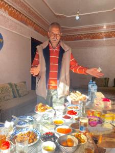 um homem parado em frente a uma mesa cheia de comida em Dar Imoughlad em Marrakech