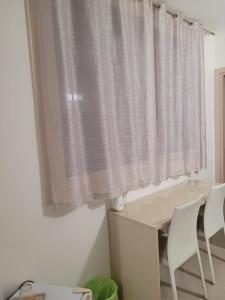 Zimmer mit einem Fenster mit weißen Vorhängen sowie einem Tisch und Stühlen in der Unterkunft Kristal in Cinisi