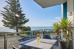 una mesa con una botella de vino en un balcón con vistas al océano en Waves on Esplanade - Kaikoura Waterfront Apartment, en Kaikoura