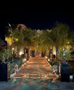 a walkway with palm trees and lights at night at Riad le Ksar de Fes in Ain Cheggag