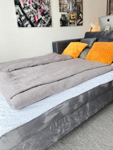 a large gray bed with orange pillows on it at Living at Saarpartments -AdultsOnly- 2 Bedrooms, Kitchen- Business & Holiday Apartments for Long- and Short term Stay, 3 min to Train-Station, Secure E-Bike Parking! in Saarbrücken