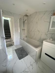 a white bathroom with a tub and a sink at Modern 3 bed flat near Crystal Palace Stadium with great transport links in Norwood