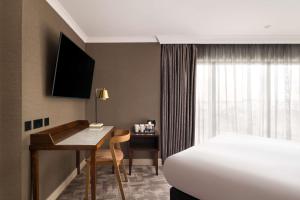 a hotel room with a bed and a desk and a bed and a bed at DoubleTree by Hilton Hotel Newcastle International Airport in Newcastle upon Tyne