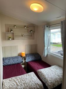 a small room with two beds and a window at 8 Bed Sun Decked Caravan Unlimited High speed Wifi and fun at Seawick Holiday Park in Clacton-on-Sea