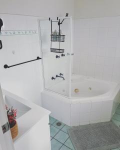 La salle de bains blanche est pourvue d'une baignoire et d'une douche. dans l'établissement Nautilus Beach Apartment Merimbula, à Merimbula