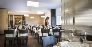 a woman standing in a dining room with tables and chairs at Hotel Excelsior - Liburnia in Lovran