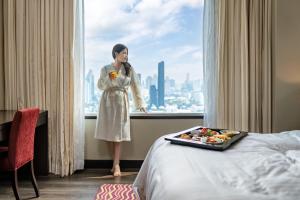 a woman standing in front of a window with a tray of food at Marriott Executive Apartments Sukhumvit Park, Bangkok in Bangkok
