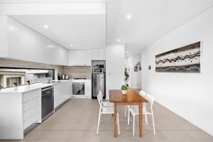 a white kitchen with a wooden table and chairs at New Modern 2BR 2baths Apt in Homebush Sleeps 6 in Sydney