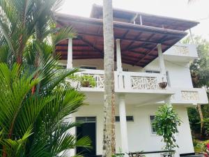 a white house with a balcony and palm trees at Susha Happy One 2BR First Floor Apartment in Hikkaduwa