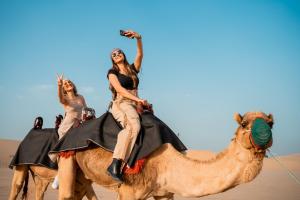 two women riding on the camel in the desert at Desert Safari Overnight Experience "Modern room with AC & Entertainment" in Hunaywah