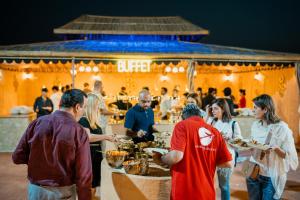 un grupo de personas comiendo en un buffet en Desert Safari Overnight Experience "Modern room with AC & Entertainment", en Hunaywah