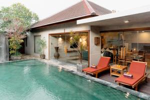 a swimming pool in front of a house with red chairs at Bracha Villas Bali - CHSE Certified in Seminyak