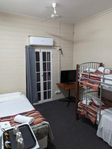 a room with two beds and a desk with a television at GRAND CENTRAL HOTEL PROSERPINE in Proserpine