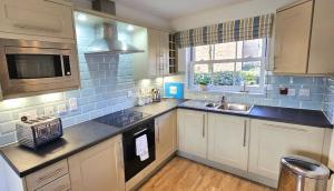 a kitchen with white cabinets and a sink and a microwave at The Bay Filey - Corner Cottage in Filey