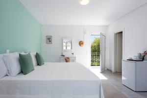 a white bedroom with a large white bed with green pillows at NiSea Apartments in Ipsos