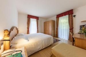 a bedroom with a bed and a desk and windows at Hotel Plank in San Martino di Castrozza