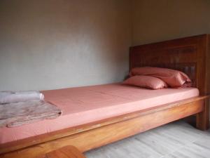 a bed with a wooden frame and pink sheets and pillows at Kadek Homestay in Besakih