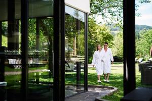 a man and a woman in white walking through a glass door at Ganischgerhof Mountain Resort & Spa in Nova Ponente