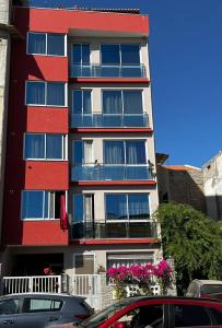 a tall red and white building with balconies and cars at AL Guesthouse in Praia