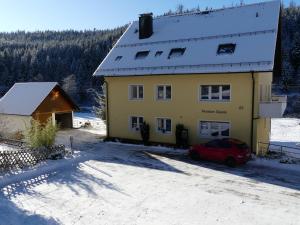 ein gelbes Haus mit einem roten Auto im Schnee in der Unterkunft Haus Gisela in Forbach