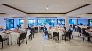 um salão de banquetes com mesas e cadeiras brancas e janelas em Hotel Samba em Lloret de Mar
