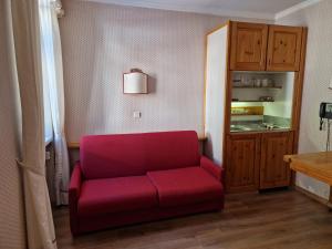 a red couch in a room with a kitchen at Villaggio Turistico Ploner - nel cuore delle Dolomiti tra Cortina e Dobbiaco in Dobbiaco