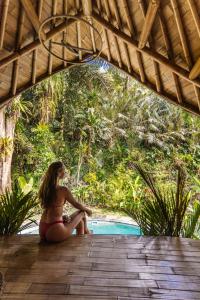 Eine Frau im Bikini, die auf einem Deck neben einem Pool sitzt. in der Unterkunft Bamboo House - Ecobreeze in Sidemen