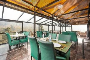 a restaurant with green chairs and tables and windows at Marina Drung Waterfall By Stay Pattern in Gulmarg