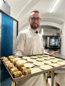 Um homem de pé numa cozinha com uma bandeja de bolachas. em Historico Loft & Rooms Palazzo Adragna XIX em Trapani