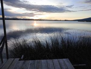 puesta de sol sobre un lago con muelle de madera en Laguna del Titicaca lodge, en Puno