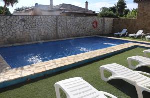 コニル・デ・ラ・フロンテーラにあるApartamento en Conil con piscinaの白い椅子2脚と石壁のスイミングプール
