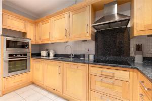 uma cozinha com armários de madeira e bancadas pretas em The Clerkenwell Flats em Greenford