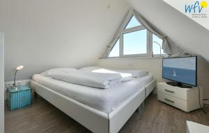 a white bedroom with a bed and a television at Bootshaus in den Duenen - 4 "Ferienwohnung Duenenkoje" in Wangerooge