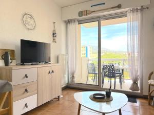 ein Wohnzimmer mit einem TV, einem Tisch und einem Balkon in der Unterkunft Appartement Le Lavandou, 1 pièce, 3 personnes - FR-1-251-420 in Le Lavandou