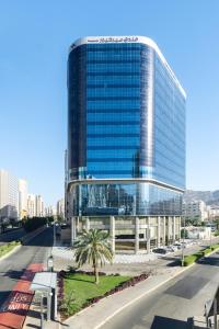 a large glass building with a palm tree in front of it at Mercure Makkah Aziziah in Makkah