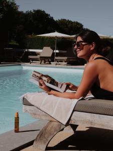 a woman sitting next to a pool reading a book at Résidence & Hôtel Aria Marina in Propriano