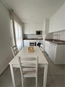 アルムニェーカルにあるApartamentos Turísticos Victoriaの白いキャビネット、白いテーブルと椅子付きのキッチン